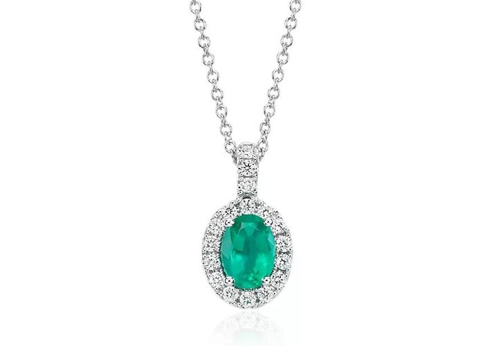 An oval-cut emerald pendant features a white diamond halo on a white gold chain